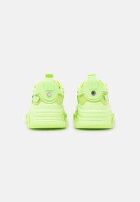Neonowe zielone sneakersy z teksturowanym górnym materiałem z siateczki, gumową podeszwą i tylnymi uchwytami. Posiadają okrągłe akcenty w pobliżu pięty.