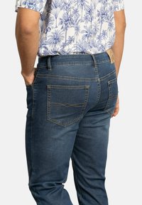 Jeans de mezclilla azul oscuro con corte recto, que cuentan con dos bolsillos traseros con costuras detalladas y una etiqueta de cuero en la cinturilla.