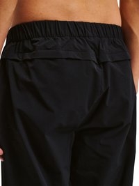 Talje og hofter på person iført sorte elastiske bukser, der viser syningsdetaljer samt delvist nedre ryg og hånd.