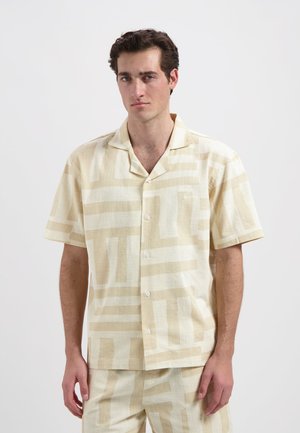 Korte mouwen, lichtbeige shirt van een gestructureerde stof, met een geometrisch crème patroon en een kraag. Witte knopen sieren de voorkant.