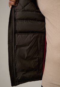 Black padded jacket interior with quilted design, featuring multiple pockets and a contrasting red lining. Soft, smooth texture.