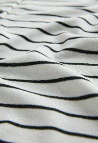 Bílá tkanina s černými horizontálními pruhy, která má jemný, texturovaný vzhled a vlnitý spád, zdůrazňující vzor pruhů.
