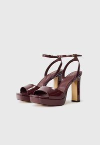 Burgundy lackläder plattformssandaler med öppen tå, ankelrem och hög klack. Slät yta med en glänsande finish.