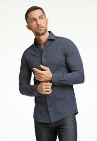 Mörkblå skjorta med knappar och långa ärmar, tillverkad av strukturerad tyg, med en något öppen krage och figursydd design.