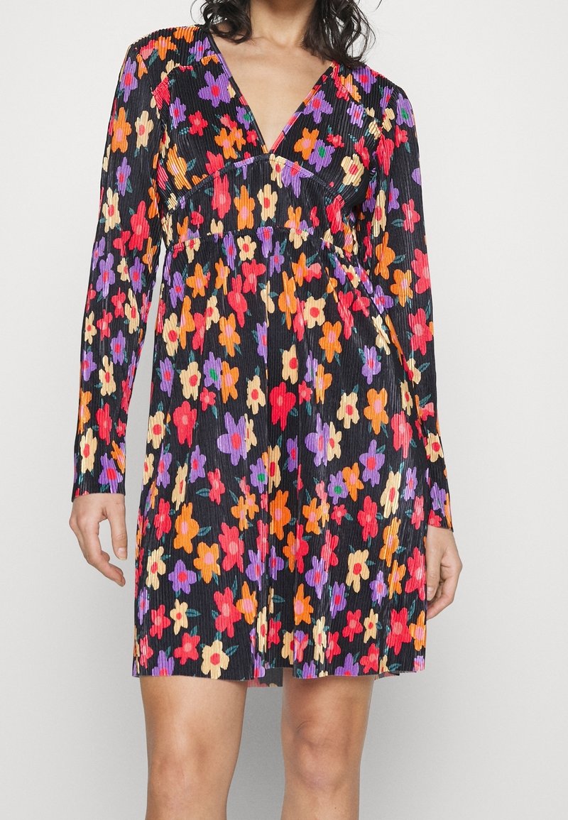 Robe florale avec un fond noir et des fleurs colorées en rouge, rose, violet et orange. Texture plissée, manches longues et décolleté en V.