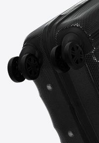 Harde koffer van zwart textuurmateriaal; voorzien van twee zwarte spinner wielen en een ritssluiting. Het ontwerp bevat zichtbare hardware accenten.