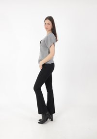 Top gris de manga corta con un ajuste relajado, combinado con jeans negros de pierna acampanada y botas negras de tobillo. Líneas limpias y silueta moderna.