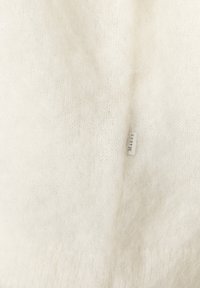 Sanfter, flauschiger, cremefarbener Strickstoff mit einer zarten Textur. Ein kleines Etikett ist sichtbar und verleiht dem Design Details.