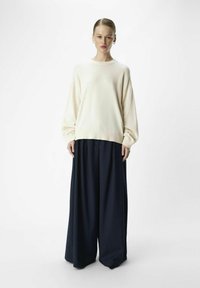 Cremefarvet strikket sweater med drop skuldre, parret med vide navy bukser. Glat tekstur, afslappet pasform og minimal design.