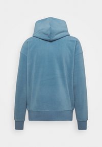 Sweat à capuche en tissu bleu doux, doté d'une coupe décontractée, de poignets côtel és et d'un design simple sans logos ni motifs visibles.