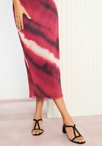 Punane ja valge batikmuster midi kleit kitsas silueti ja läbipaistva servaga. Mustad T-sandaalid väikese kandiga. Siledad tekstuurid.