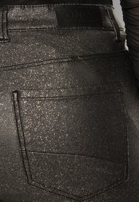 Černé džíny z denimu s třpytivou texturou, obsahující zadní kapsu a nášivku "ONLY" na pásku. Jemný třpytivý detail.