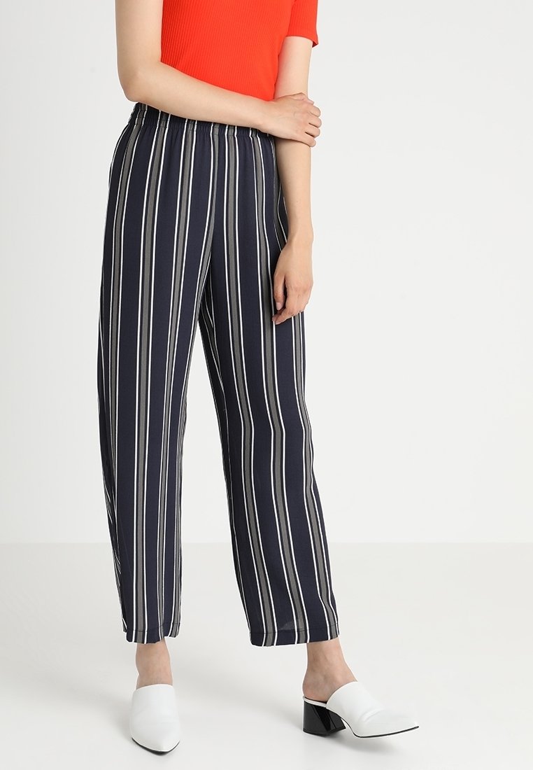 Person som bär marinblå byxor med vertikala vita ränder, en orange kortärmad topp och vita klackskor.