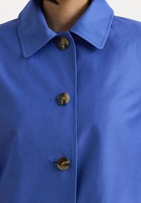 Camisa azul con botones, que cuenta con cuello, tela suave y botones marrones. Destaca por su diseño sencillo y líneas limpias.