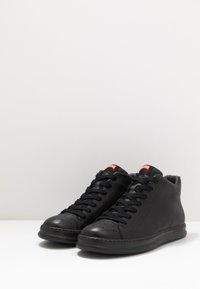 Sorte høyde sneakers laget av lær med en glatt tekstur. Har rundt tå, polstret krage og lisser. Rødt merkelapp på tungen.
