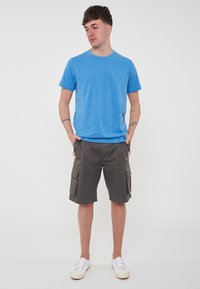 T-shirt azzurro chiaro a maniche corte in un materiale morbido, abbinato a pantaloni cargo grigi lungo il ginocchio con tasche laterali e una vestibilità rilassata.