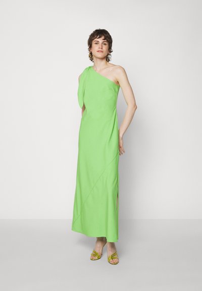 Πράσινο, μονόχωρο μάξι φόρεμα με ριχτή σχεδίαση, πλαϊνές σχισμές και λεία υφή. Φορεμένο με κίτρινες σανδάλες με λουριά και υπερμεγέθη σκουλαρίκια.