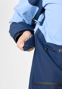 Navy- und hellblaue wasserdichte Jacke mit mehreren Knöpfen, verstellbaren Bündchen und einer Reißverschlusstasche. Glatte Textur mit funktionalem Design.