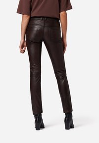 Bruine leren broek met een slim fit, voorzien van achterzakken, subtiele stikdetails en een zachte textuur, gecombineerd met zwarte hoge hakken.