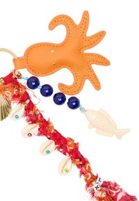 Pomarańczowa zawieszka ośmiornicy wykonana z teksturowanego materiału, ozdobiona złotym przeszyciem. Zawiera niebieskie koraliki, ryby i muszle kauri na czerwonym pasmie z tkaniny.