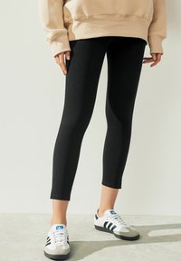 Mustad mustad leggings, veniv kangast, kitsas disain, täispikkus, kombineeritud mustade ja valgete tossudega, millel on sinine logo aktsent.