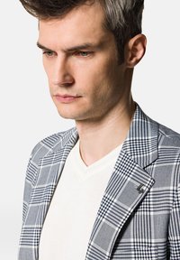 Wzorzysta marynarka w niebiesko-białą kratę z klapą, połączona z białym podkoszulkiem w szpic. Teksturowany materiał z subtelnymi detalami.