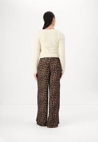 Personne avec des cheveux tressés portant un pull crème à manches longues et un pantalon large à taille haute avec imprimé léopard, de dos.