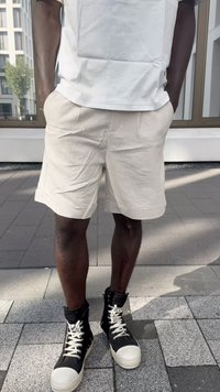 Beige linen shorts feature front pockets and cuffed hems. Paired with black high-top sneakers with white soles and laces.
