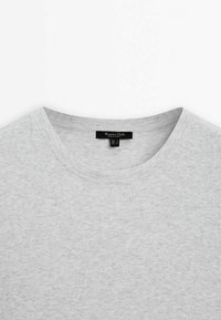 Grå ribbet t-shirt med rund halsudskæring. Mærket er sort og syet ind i kraven. Stofstrukturen virker blød og let.