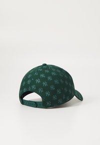 Grön keps med upprepande NY-logotypmönster, strukturerad design, böjd skärm och justerbar snapback-stängning bak.