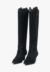 Černé semišové kozačky po kolena s špičatou špičkou, vlnitým vrškem a jemnými švy. Mají nízký podpatek pro větší stabilitu.