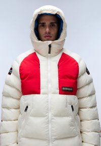 Giacca imbottita caratterizzata da un corpo crema con pannelli frontali rossi. Chiusura a zip, cappuccio e due tasche laterali con zip. Logo sul petto.