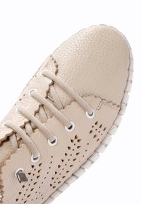 Sneaker in pelle beige con finitura testurizzata, bordi scallopati, design perforato e lacci bianchi; presenta una suola traslucida.