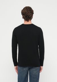 Czarna koszula z długim rękawem i okrągłym dekoltem. Miękki materiał, dopasowany krój. Noszona z niebieskimi jeansami typu denim. Prosta, bez widocznych wzorów ani dodatków.