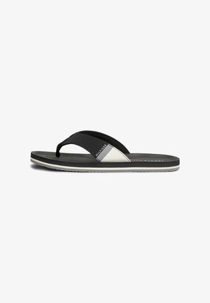 Sort-hvide Tommy Hilfiger flip-flop sandaler med enkelt thongsrem og flad sål, vist fra siden på en hvid baggrund.
