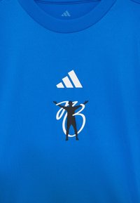 Modrá sportovní tričko vyrobené z hladkého materiálu s bílým logem Adidas a černým siluetovým grafickým prvkem s stylizovaným textem pod ním.