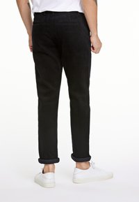Pantalones de pana negros con corte recto, puños enrollados y bolsillos. Combinados con zapatillas blancas, mostrando una superficie de tela texturizada.