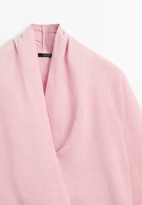 Lichtroze linnen wikkel-top met diepe V-hals en een klein zwart labeltje aan de binnenkant van de kraag.