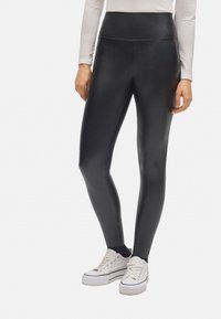 Leggings de imitación cuero negro con una cinturilla alta, textura suave y una silueta ajustada, combinados con zapatillas blancas.