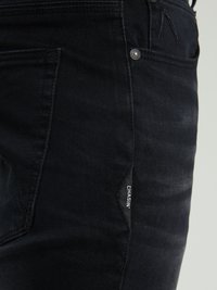 Crne traperice od denim materijala koje imaju uski kroj, božnu oznaku, detalje od metalnog dugmeta i suptilnu teksturu s lagano izblijedjelim finišem.