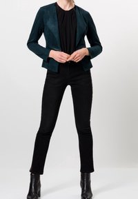 Turkooise suède jas met een getailleerd ontwerp, een reverskraag en lange mouwen, gecombineerd met zwarte skinny jeans en enkellaarsjes.