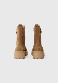 Botines de ante color tostado con una superficie texturizada, que cuentan con una suela media gruesa y cremalleras laterales para facilitar su uso.