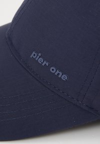 Casquette bleu marine en tissu texturé avec une visière incurvée. Logo "pier one" en relief à l'avant. Accents cousus le long des coutures.
