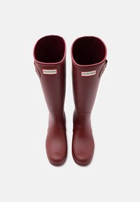 Raudoni guminiai lietaus batai su blizgiu paviršiumi, tiesia forma, apvaliu pirštu ir logotipo akcentais viršuje. Vidus išklotas minkšta medžiaga.