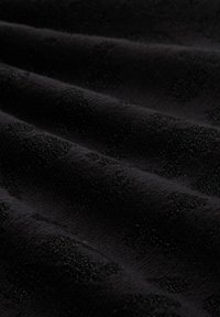 Zwarte stof met subtiele, verhoogde fluwelen polkadots die een textuurpatroon vormen op een glad oppervlak.