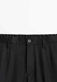 Zwarte broek met een platte tailleband, elastische achterkant en knoopsluiting aan de voorkant. Voorzien van twee zijzakken en een gladde stoftextuur.