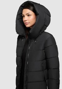 Zwarte pufferjack met een grote capuchon, voorzien van een quilted ontwerp, voorrits en zijzakken. Een gladde textuur met een strakke afwerking.