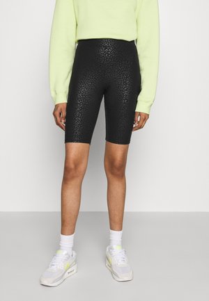 Svarta cykelbyxor med ett subtilt leopardmönster, gjorda av stretchmaterial, kombinerat med en ljusgrön sweatshirt och vita sneakers.