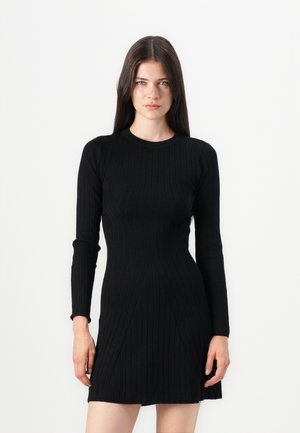 Abito a maglia a coste nera con maniche lunghe, scollatura rotonda, silhouette aderente e dettagli a pannello per la forma. Texture liscia e lunghezza sopra il ginocchio.