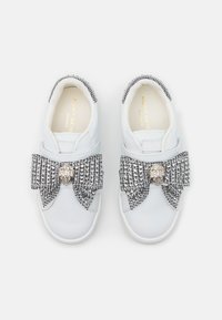 Baskets blanches avec un grand nœud en pied-de-poule noir et blanc, orné d'un accent métallique au centre. Tige en cuir lisse et semelle en caoutchouc.